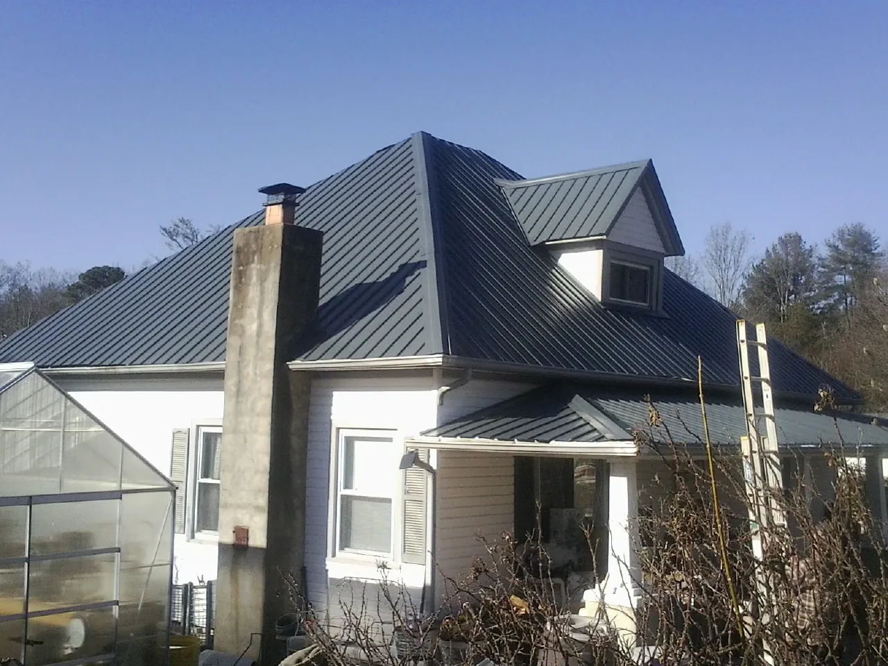 Dark blue standing seam metal roof on a white farmhouse with dormer — Slate & Tile Roof Repair by Roofing Brothers in Grandin