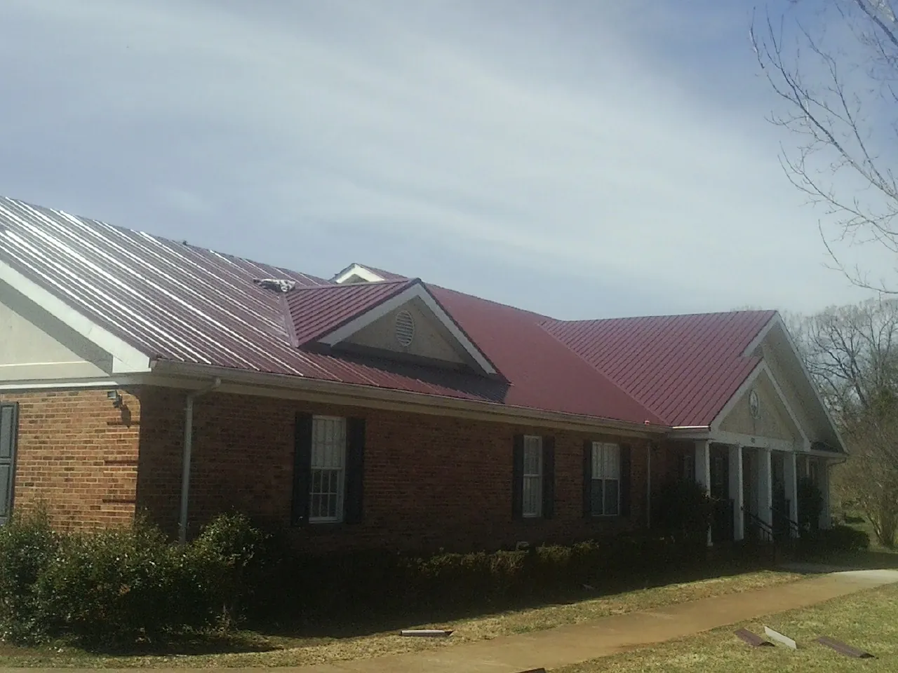 Red metal roof with gabled entries on a long brick building, from a Hail Damage Roof Repair job in Grandin