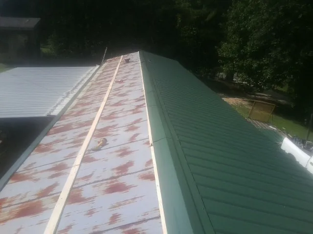 Old rusted panels beside newly installed green metal roofing — Wind Damage Roof Repair by Roofing Brothers in Grandin