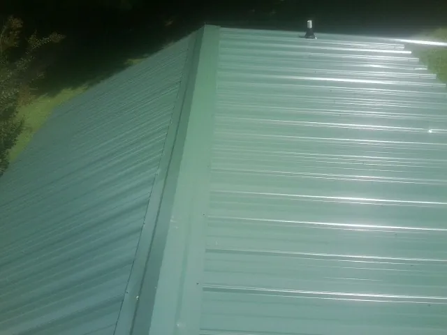New green metal panels meeting at the ridge of a roof — Flat Roof Repair work by our crew in Grandin
