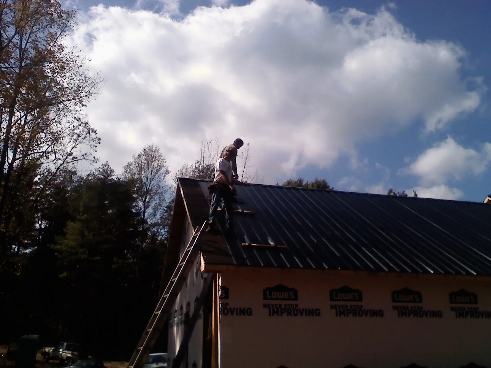 Roofer fastening dark metal panels high against a cloudy sky, from a Roof Inspection job in Grandin