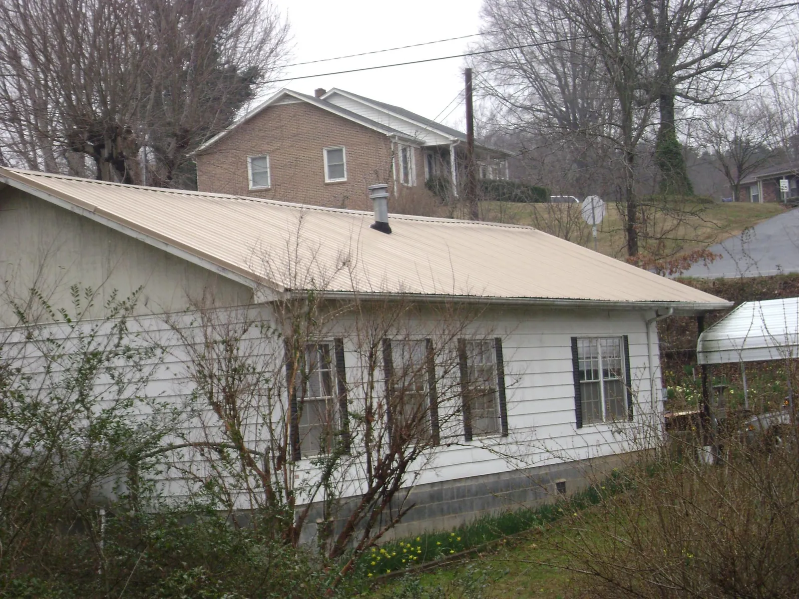 Tan metal roof on a white sided house set into a hillside — Commercial Roofing by Roofing Brothers in Grandin