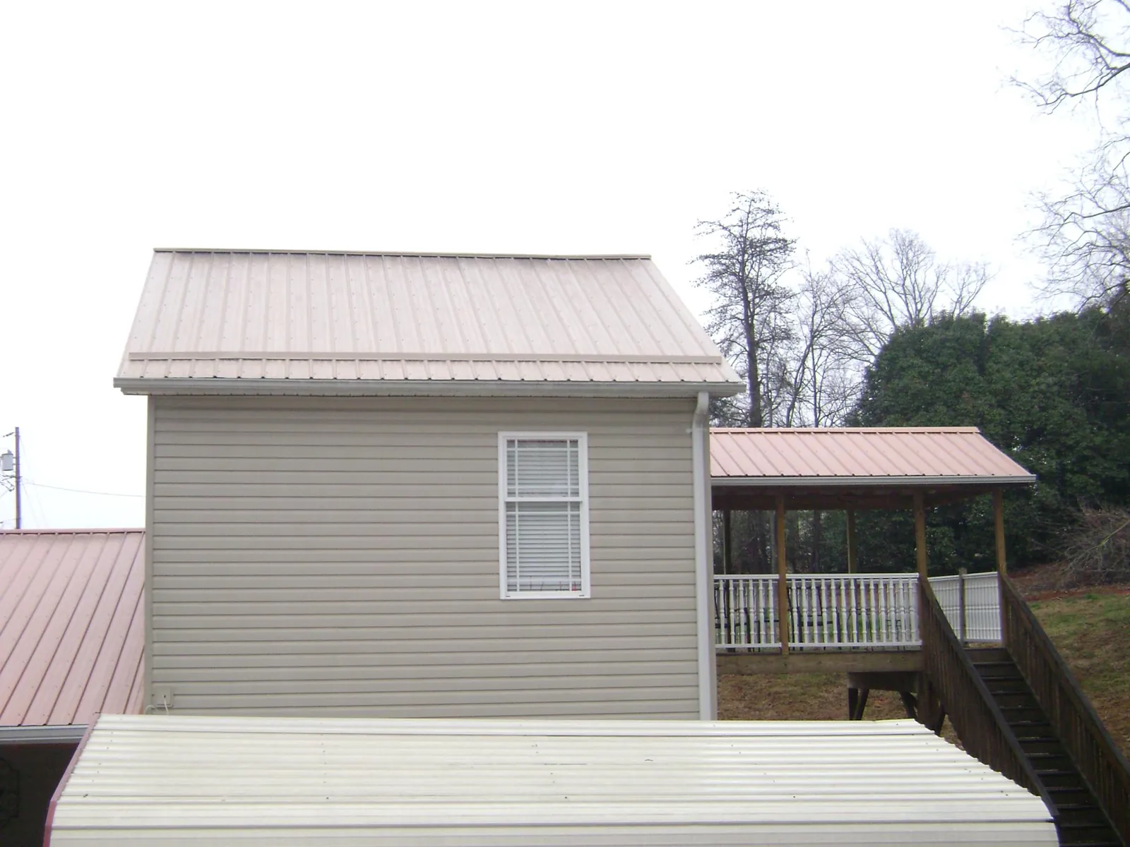 Tan metal roofs on a two story addition and attached porch, from a Roof Replacement job in Grandin